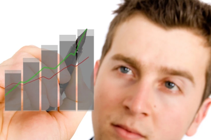 A man is drawing upward-trending lines on a transparent bar graph, suggesting financial or business growth. The graph is in the foreground, while the man's face is slightly out of focus in the background.
